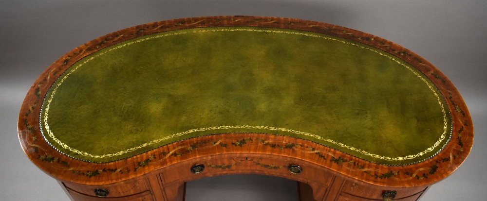 An Edwardian satinwood kidney-shaped writing desk featuring nine hand-painted drawers with brass ring handles and tapered legs on castors. View VI