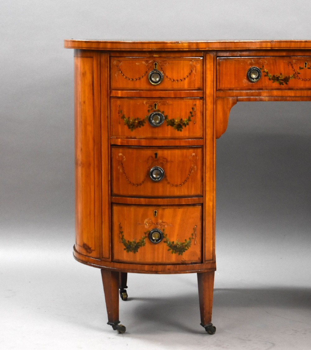 An Edwardian satinwood kidney-shaped writing desk featuring nine hand-painted drawers with brass ring handles and tapered legs on castors. View VII