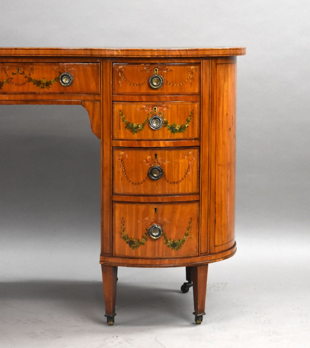 An Edwardian satinwood kidney-shaped writing desk featuring nine hand-painted drawers with brass ring handles and tapered legs on castors. View IX