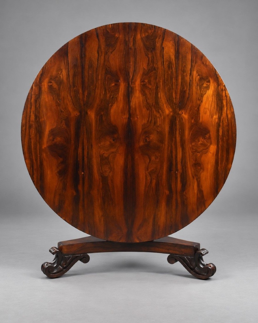 A William IV circular rosewood tilt-top breakfast table showing a book-matched grain pattern displayed vertically above a triform base.