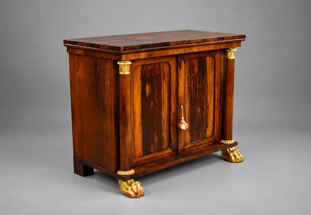 A 19th-century Regency rosewood side cabinet featuring two panelled doors, flanking column supports, and carved giltwood lion paw feet.