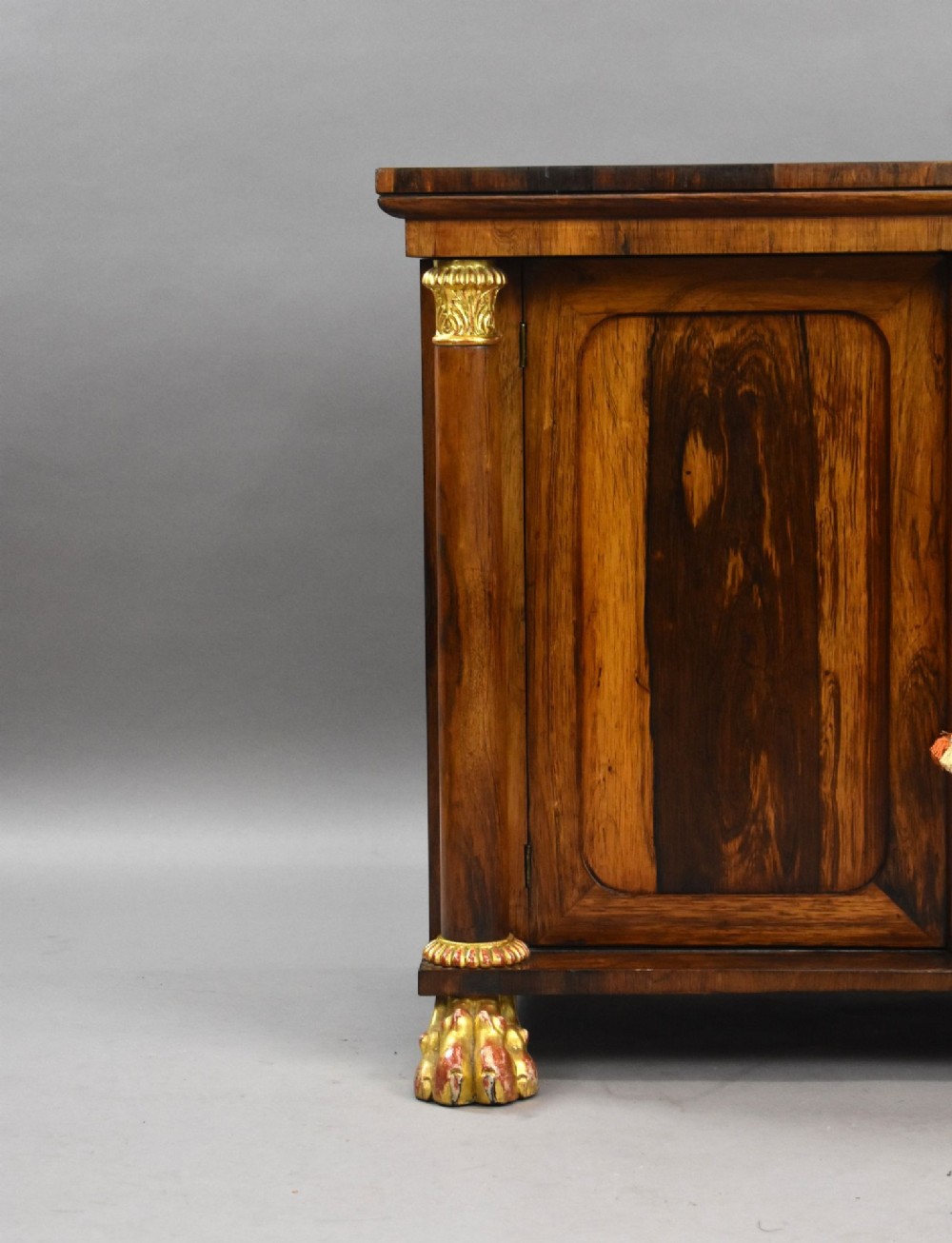 A 19th-century Regency rosewood side cabinet featuring two panelled doors, flanking column supports, and carved giltwood lion paw feet. View VI
