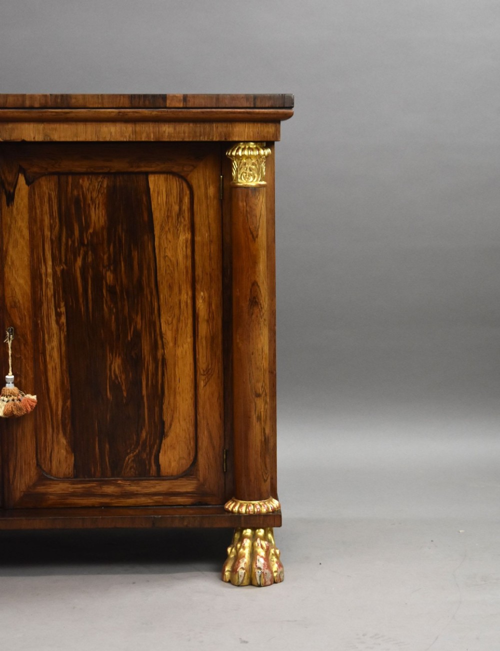 A 19th-century Regency rosewood side cabinet featuring two panelled doors, flanking column supports, and carved giltwood lion paw feet. View VII