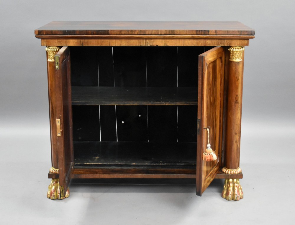 A 19th-century Regency rosewood side cabinet featuring two panelled doors, flanking column supports, and carved giltwood lion paw feet. View VIII