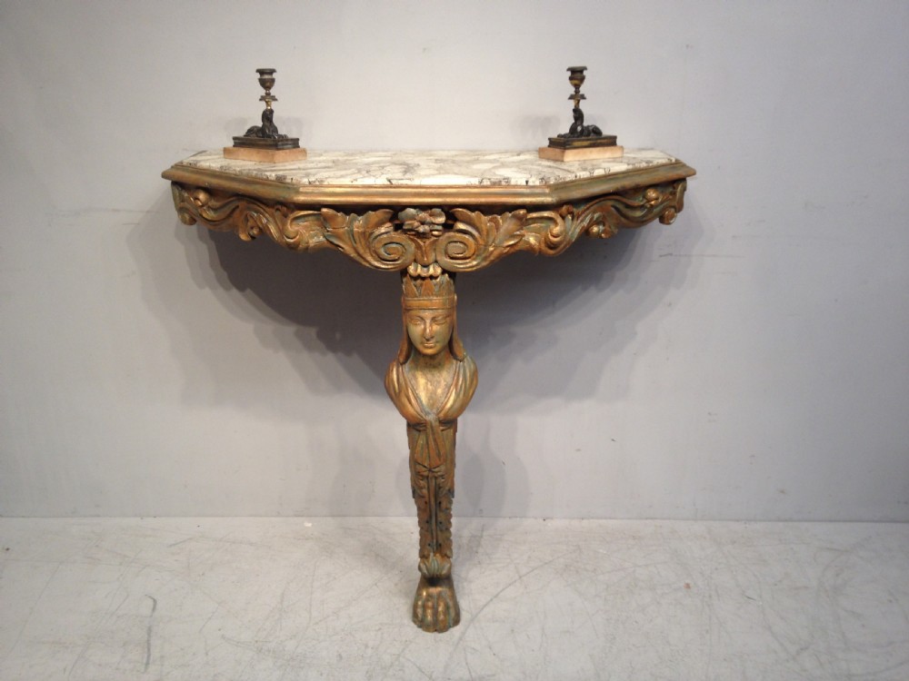 An antique carved giltwood console table featuring a single caryatid monopodium leg, scrollwork apron, and a white veined marble top.