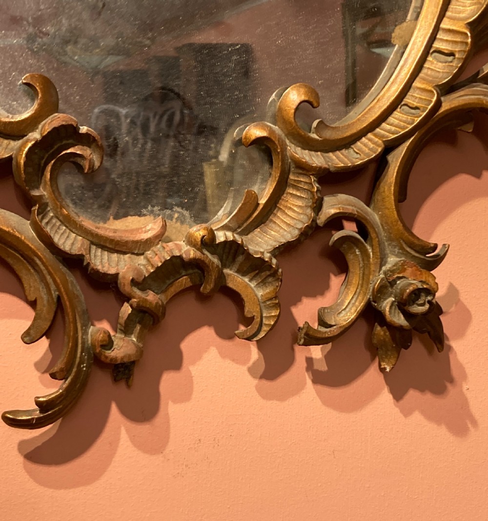 An oval wall mirror featuring an ornate, pierced carved giltwood frame with scrollwork and floral details. View III