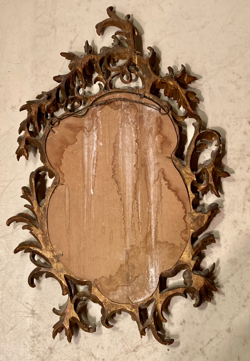 An oval wall mirror featuring an ornate, pierced carved giltwood frame with scrollwork and floral details. View V