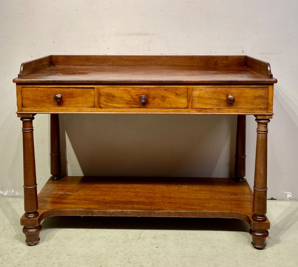 A William IV mahogany dressing table featuring a low gallery back, three frieze drawers with wooden knobs, turned legs, and a fitted lower undertier shelf.