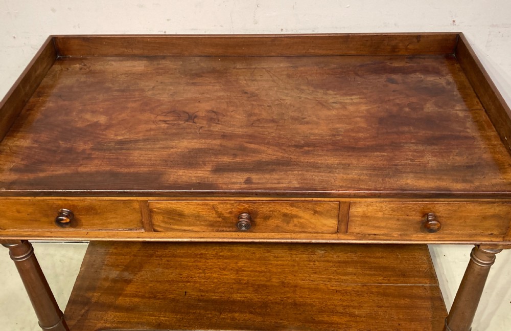 A William IV mahogany dressing table featuring a low gallery back, three frieze drawers with wooden knobs, turned legs, and a fitted lower undertier shelf. View II