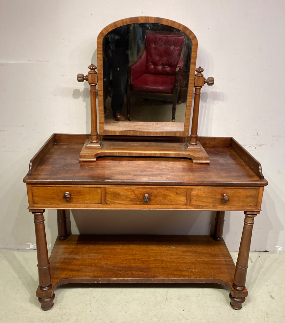 A William IV mahogany dressing table featuring a low gallery back, three frieze drawers with wooden knobs, turned legs, and a fitted lower undertier shelf. View IV