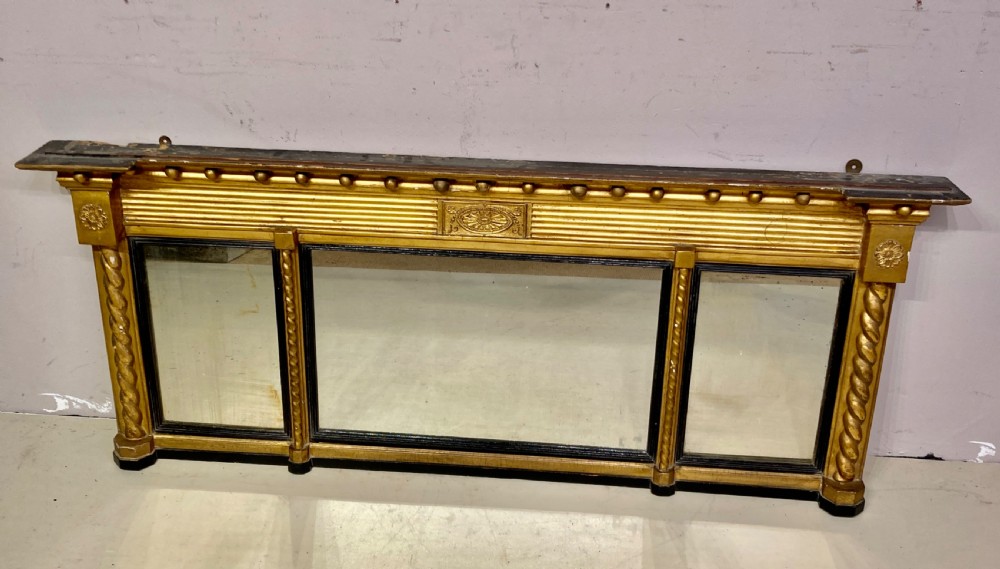A horizontal Regency period giltwood overmantel mirror featuring a three-plate glass layout, spiral-twist side columns, a ball-frieze upper cornice, and ebonised inner borders.