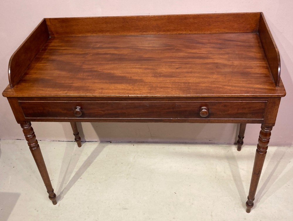 A freestanding antique Georgian mahogany writing desk featuring a raised gallery back, two drawers with turned wooden knobs, and turned tapering legs. View III