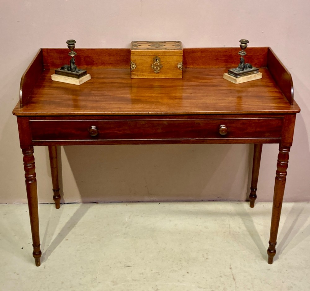 A freestanding antique Georgian mahogany writing desk featuring a raised gallery back, two drawers with turned wooden knobs, and turned tapering legs. View VII