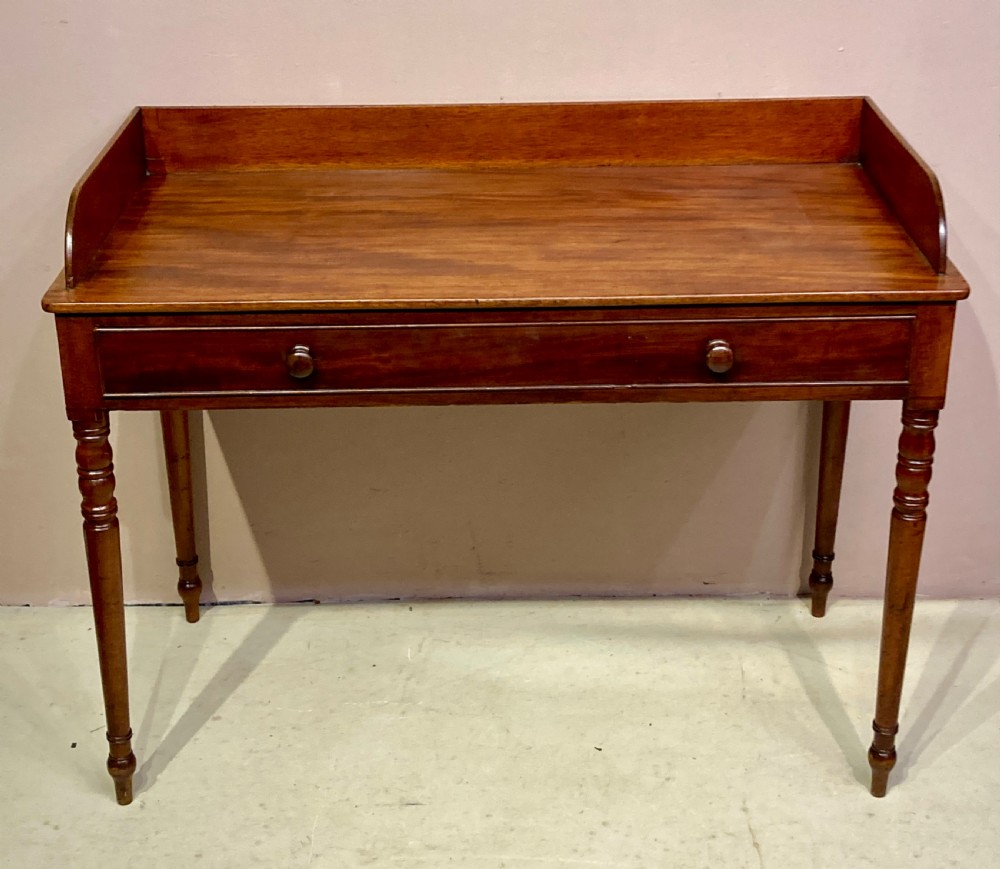 A freestanding antique Georgian mahogany writing desk featuring a raised gallery back, two drawers with turned wooden knobs, and turned tapering legs. View VIII
