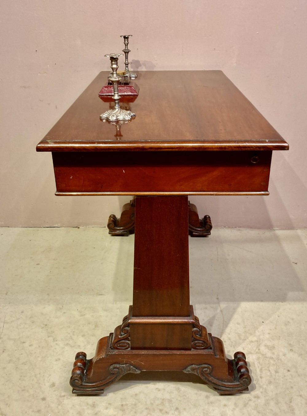 A rectangular Victorian mahogany writing table featuring a flat top, three frieze drawers with turned wooden knobs, and twin scrolling pedestal supports connected by a stretcher base. View II