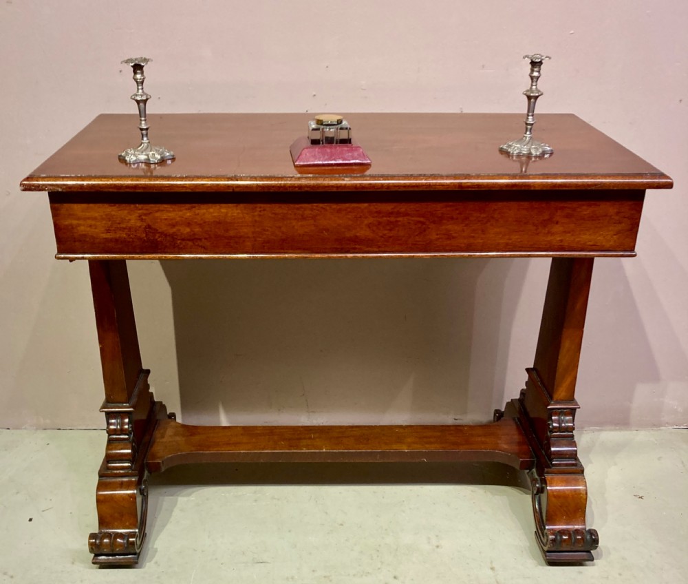 A rectangular Victorian mahogany writing table featuring a flat top, three frieze drawers with turned wooden knobs, and twin scrolling pedestal supports connected by a stretcher base. View III