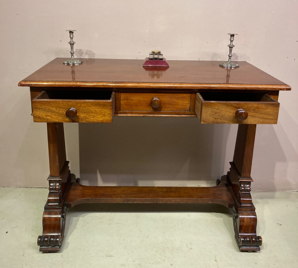 A rectangular Victorian mahogany writing table featuring a flat top, three frieze drawers with turned wooden knobs, and twin scrolling pedestal supports connected by a stretcher base. View V