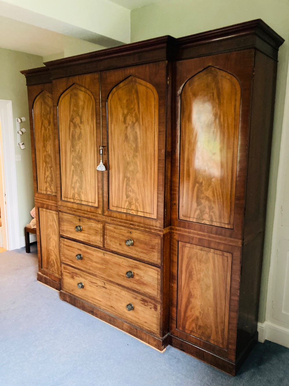 A large Georgian mahogany breakfront wardrobe featuring flame mahogany doors with pointed arch panels above a central chest of drawers.