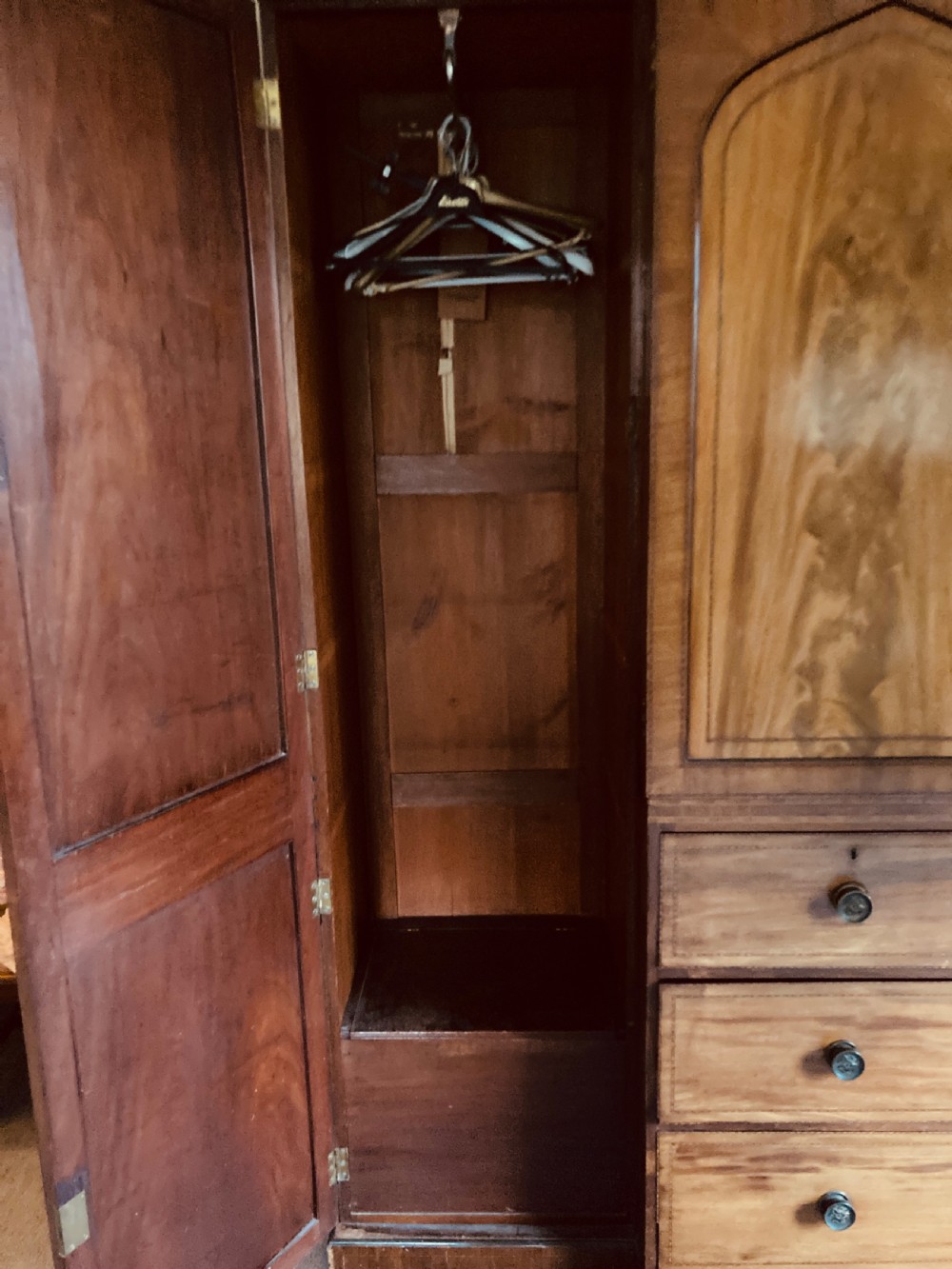 A large Georgian mahogany breakfront wardrobe featuring flame mahogany doors with pointed arch panels above a central chest of drawers. View V