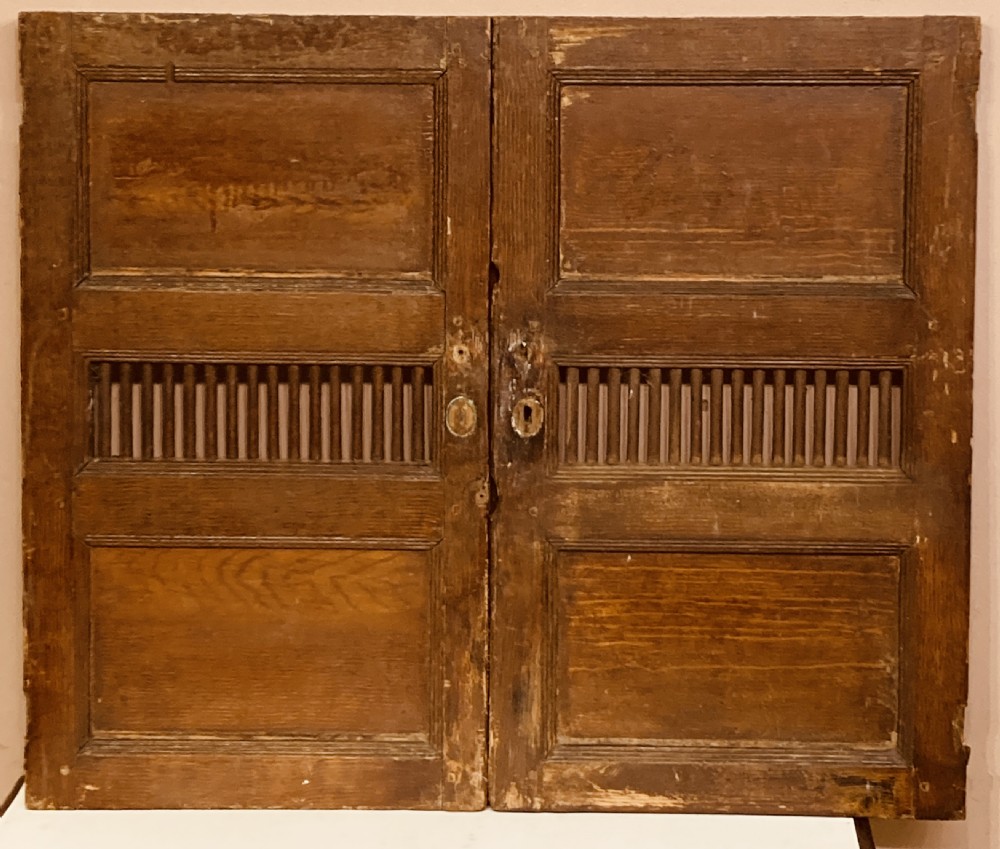 A pair of Georgian pine cupboard doors featuring a scumbled paint finish, recessed panels, central spindle grilles, and brass escutcheons.