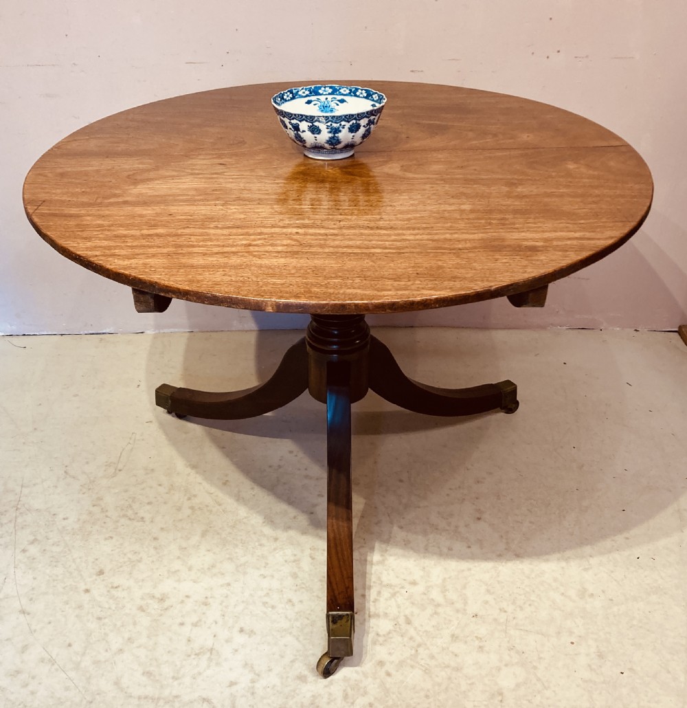 A circular mahogany table top with visible wood grain, supported by curving wooden legs ending in brass castors. View IV