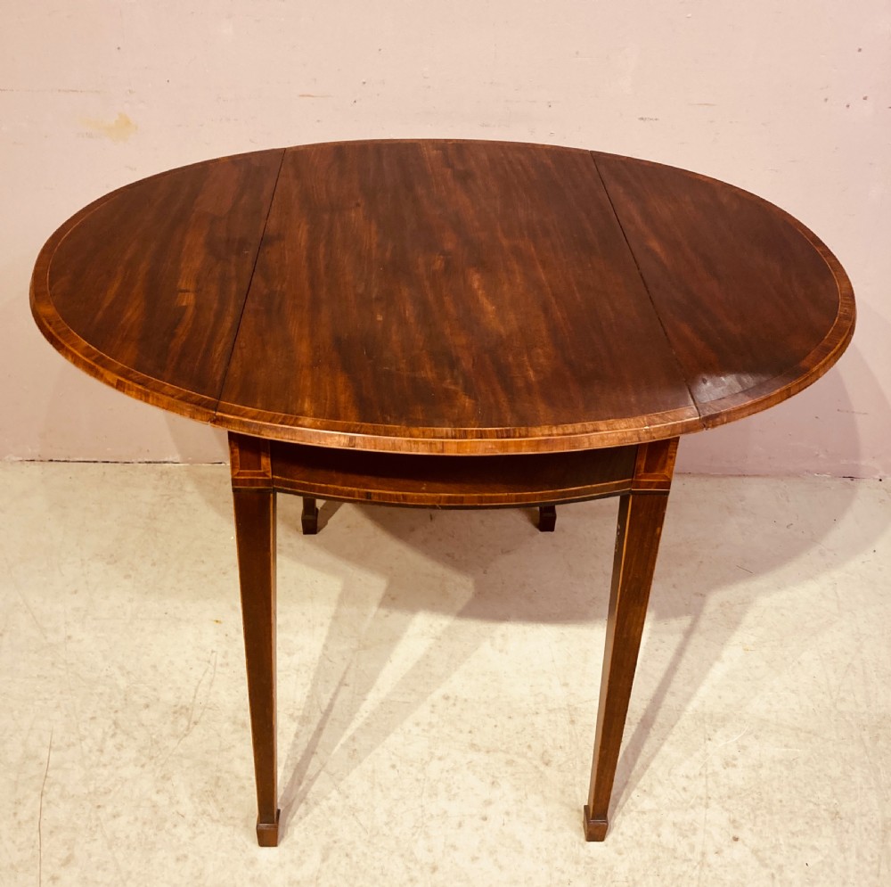 A Georgian mahogany oval Pembroke table featuring extended drop leaves, fine string inlay, a single drawer with brass ring handles, and square tapered legs. View VI