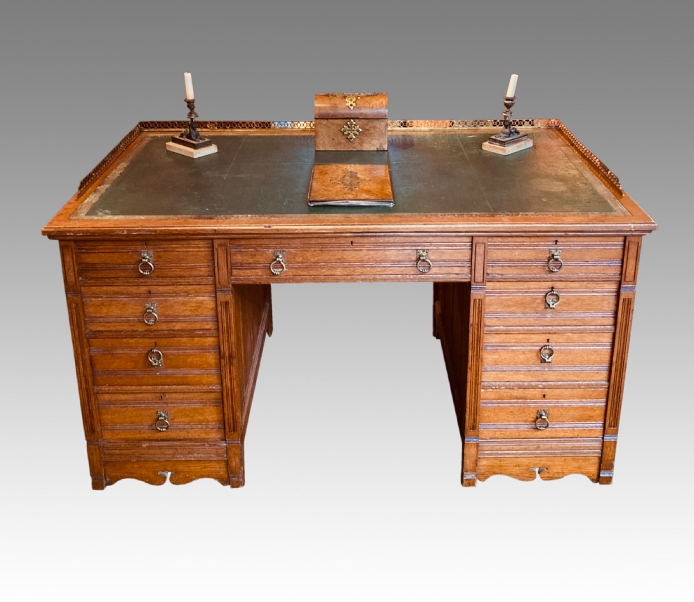 A Victorian oak pedestal desk featuring a green leather writing top, a brass gallery rail, twin banks of drawers with brass ring handles, and a central kneehole.