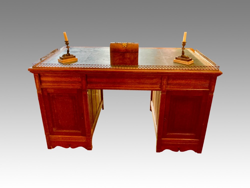 A Victorian oak pedestal desk featuring a green leather writing top, a brass gallery rail, twin banks of drawers with brass ring handles, and a central kneehole. View IV