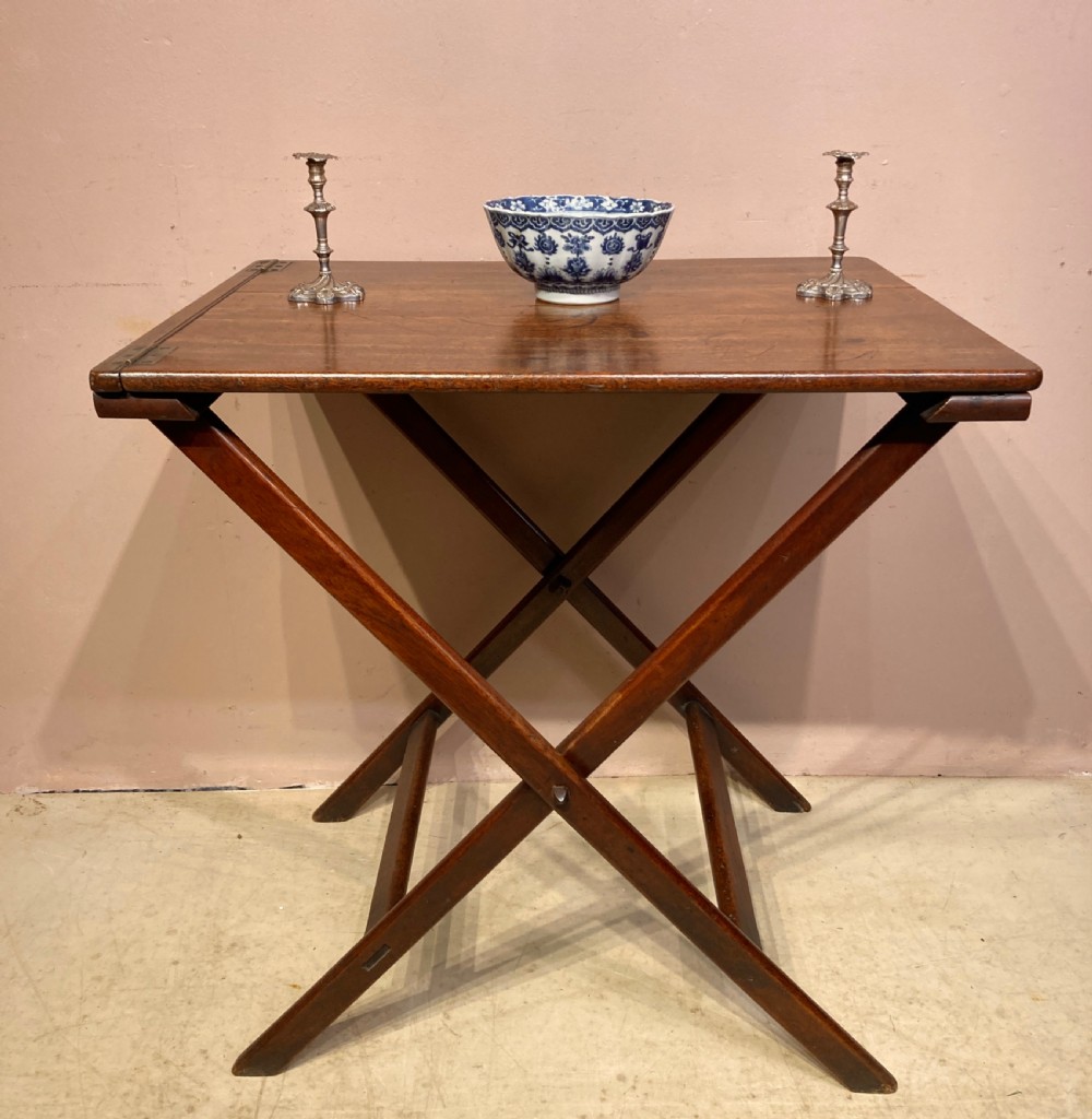 A Georgian mahogany folding butler table featuring a crossed X-frame support base and a smooth rectangular wooden top with corner brass hinges.