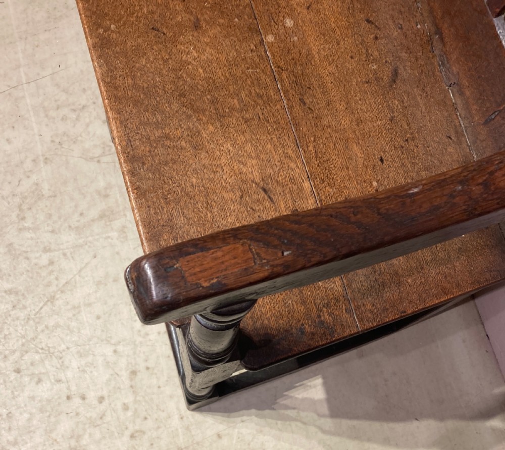 A dark carved oak wainscot armchair featuring an arched cresting rail, carved relief back panel, curved armrests, and turned legs with box stretchers. View IV
