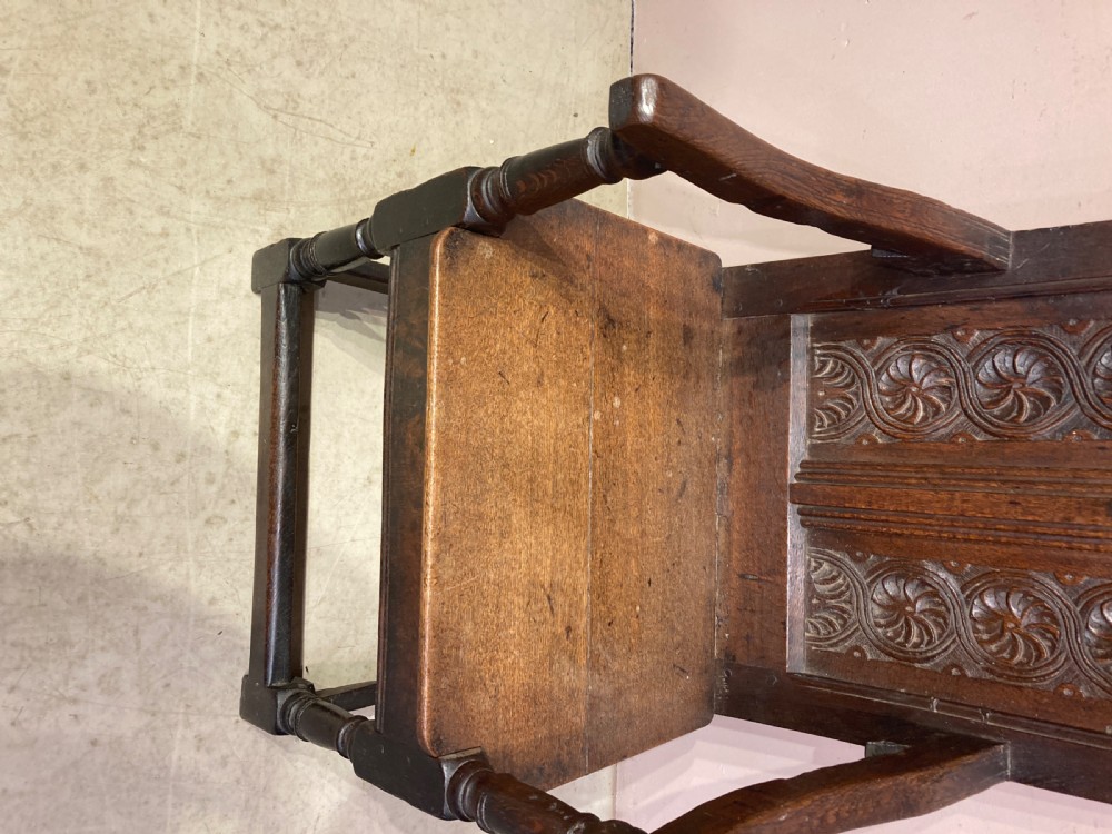 A dark carved oak wainscot armchair featuring an arched cresting rail, carved relief back panel, curved armrests, and turned legs with box stretchers. View VIII