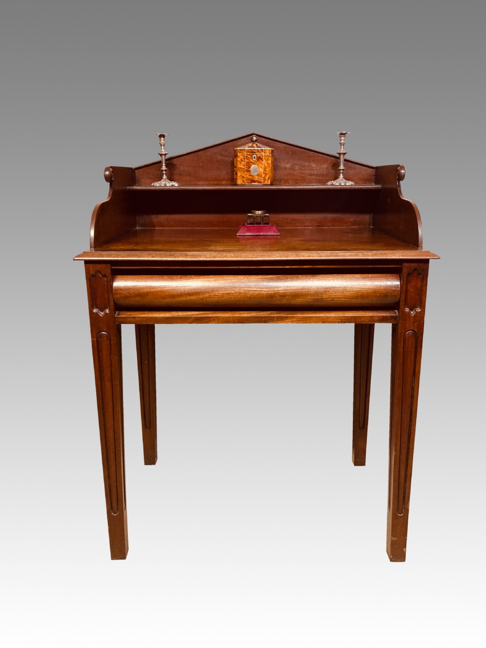 A Georgian mahogany writing table featuring a shaped gallery back shelf, a rounded tamboured front section, and square tapered legs.