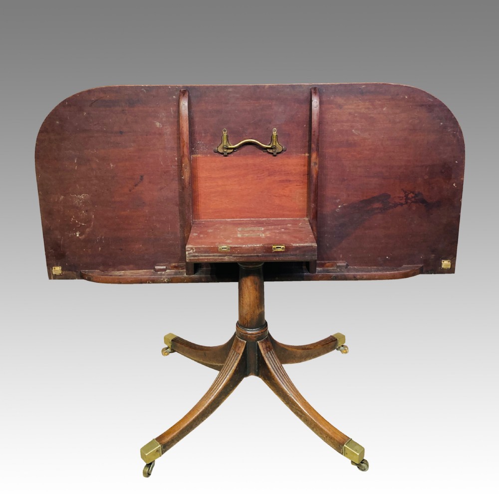 A Georgian mahogany dining table featuring a polished rectangular top with rounded corners supported by two central turned pedestals with splayed reeded legs ending in brass castors. View II