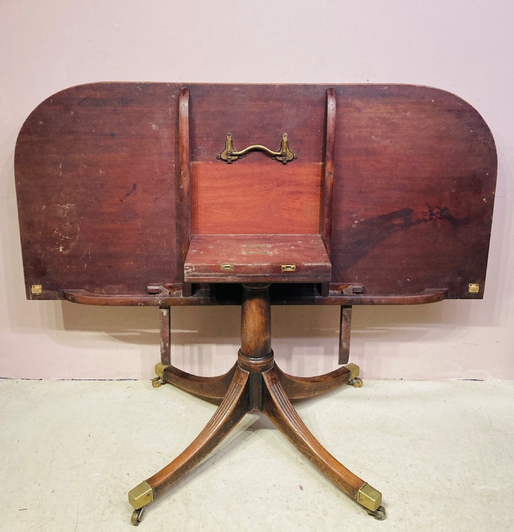 A Georgian mahogany dining table featuring a polished rectangular top with rounded corners supported by two central turned pedestals with splayed reeded legs ending in brass castors. View V