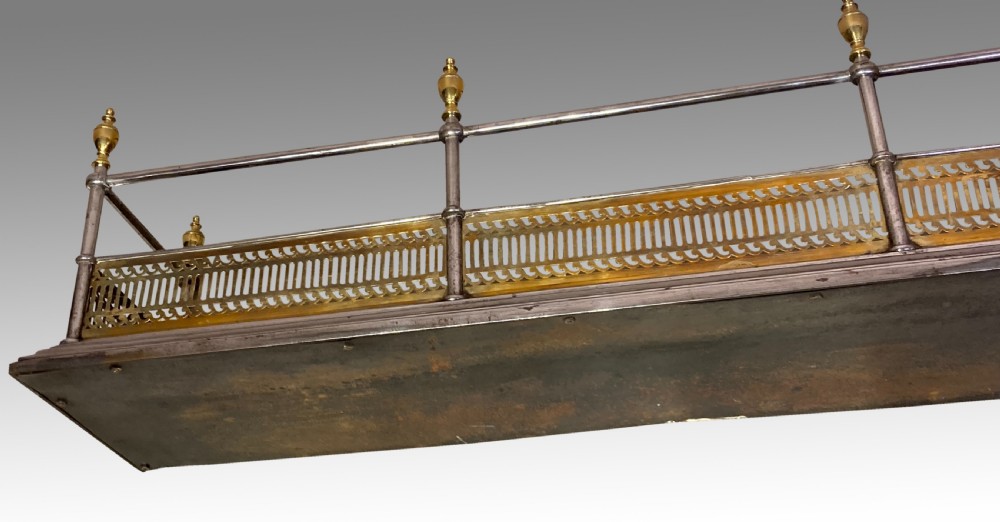 An antique polished steel hearth fender featuring a pierced brass lower gallery band, vertical support posts, and five turned brass urn finials along the top rail. View III