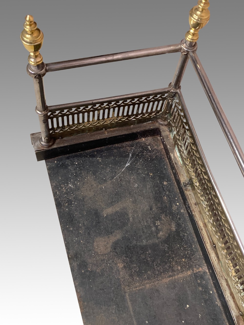 An antique polished steel hearth fender featuring a pierced brass lower gallery band, vertical support posts, and five turned brass urn finials along the top rail. View VIII