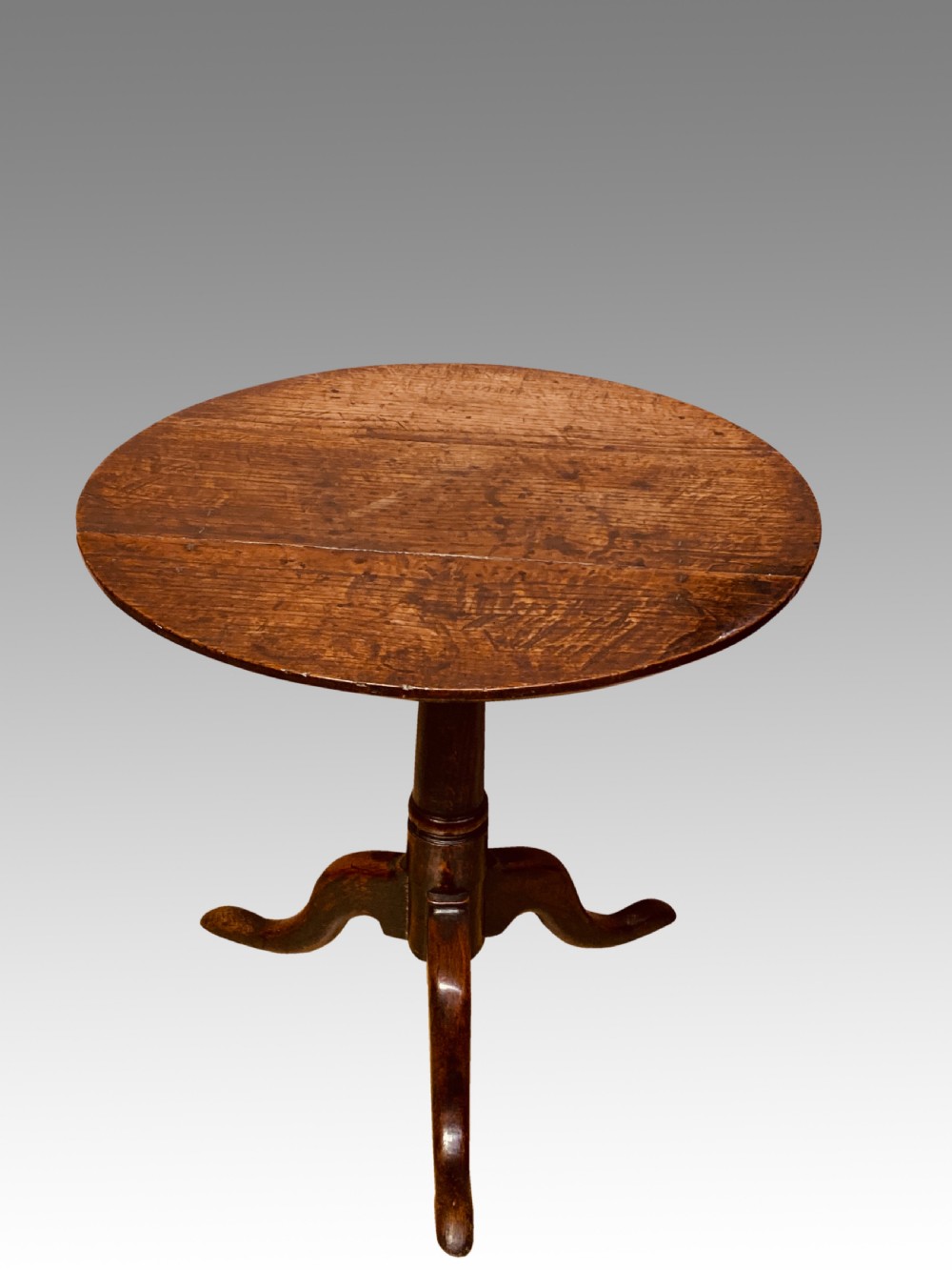 An 18th-century Georgian circular oak tripod table featuring a turned central pedestal column resting on three downswept legs.