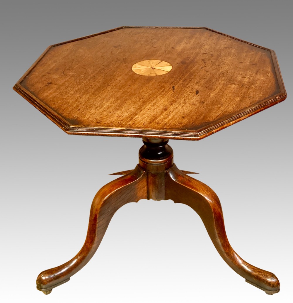 An octagonal mahogany coffee table featuring a central circular starburst inlay, a turned central column, and three curved cabriole legs on brass castors.