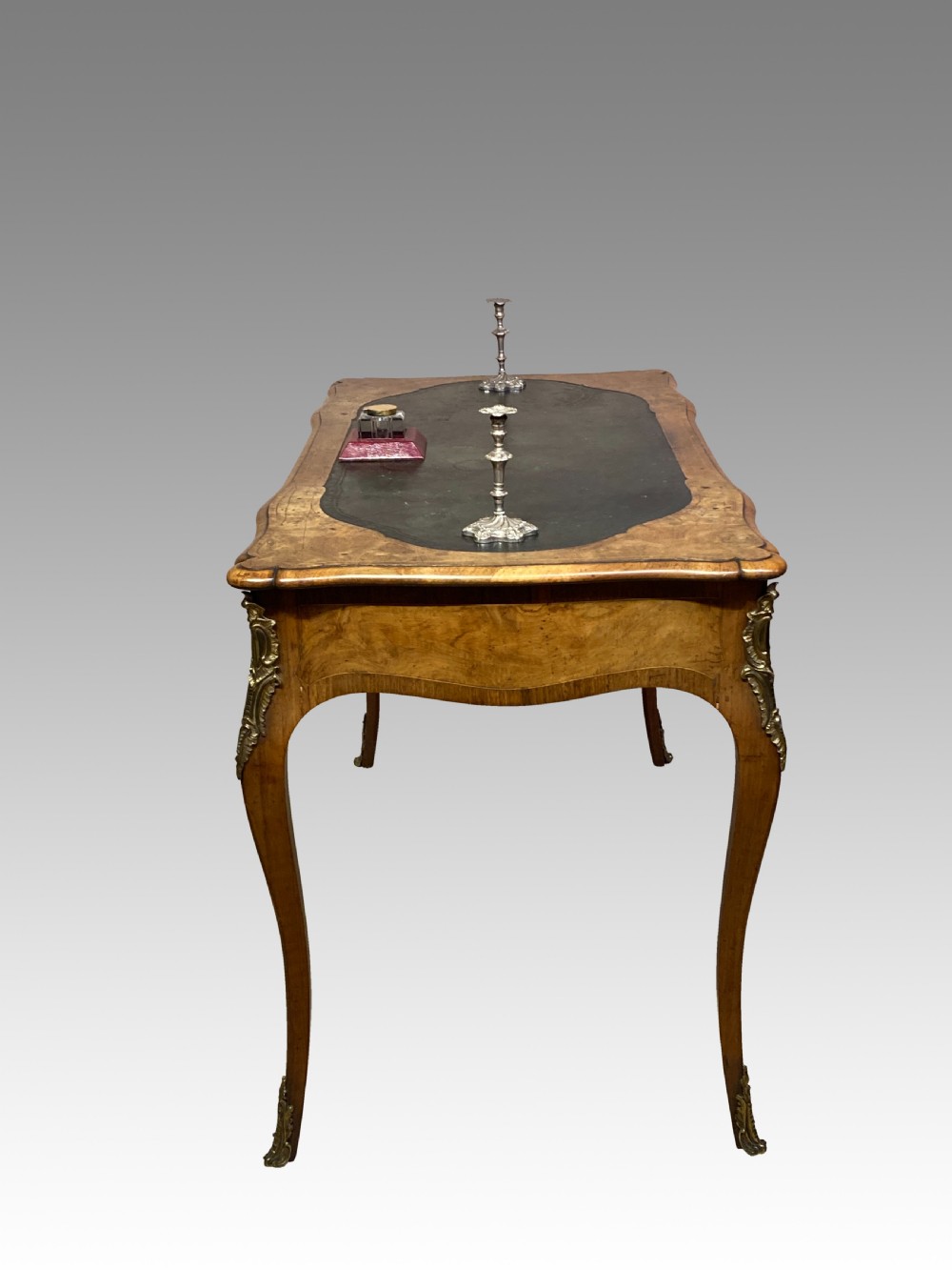 A Victorian burr walnut writing table featuring cabriole legs, ornate gilt-bronze mounts, a serpentine apron, and a dark leather inset writing surface. View III