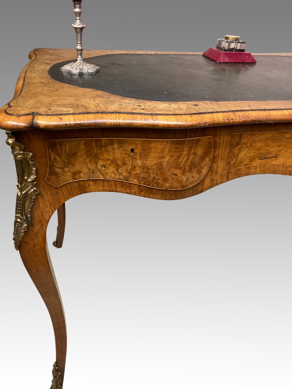 A Victorian burr walnut writing table featuring cabriole legs, ornate gilt-bronze mounts, a serpentine apron, and a dark leather inset writing surface. View VII
