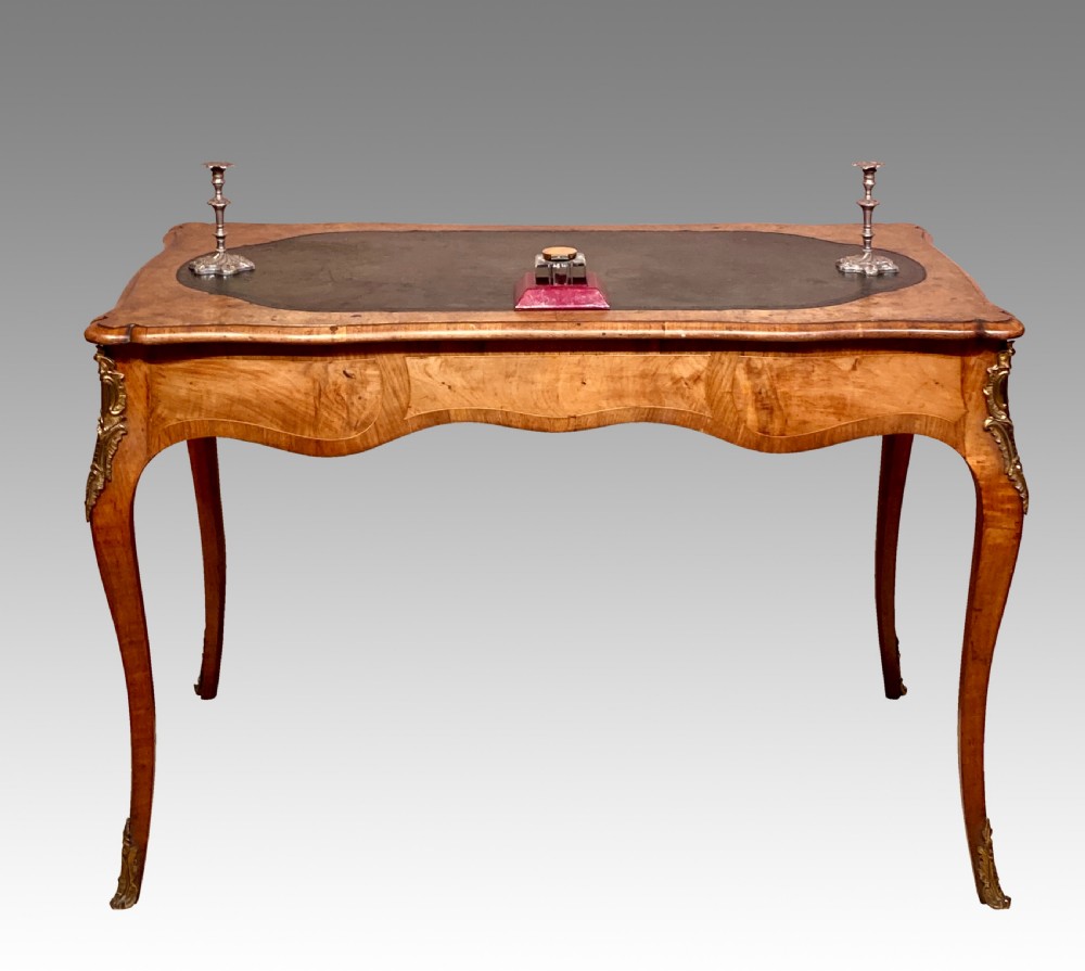 A Victorian burr walnut writing table featuring cabriole legs, ornate gilt-bronze mounts, a serpentine apron, and a dark leather inset writing surface. View VIII