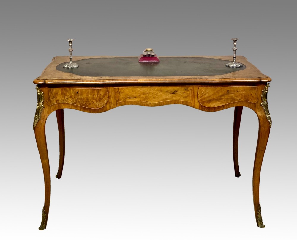 A Victorian burr walnut writing table featuring cabriole legs, ornate gilt-bronze mounts, a serpentine apron, and a dark leather inset writing surface. View IX
