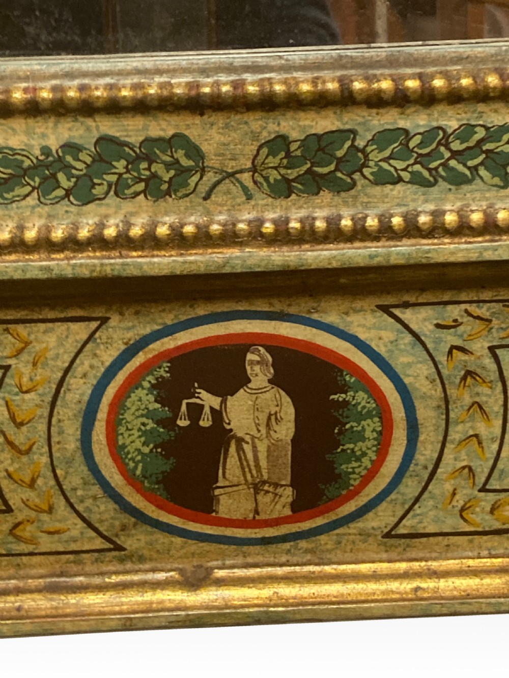 A tall Neoclassical French pier mirror featuring a green painted frame, gilded beaded trim, an urn motif cresting, and two hand-painted decorative panels. View IV