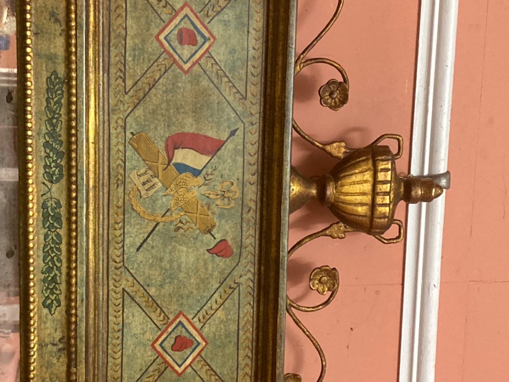 A tall Neoclassical French pier mirror featuring a green painted frame, gilded beaded trim, an urn motif cresting, and two hand-painted decorative panels. View IX