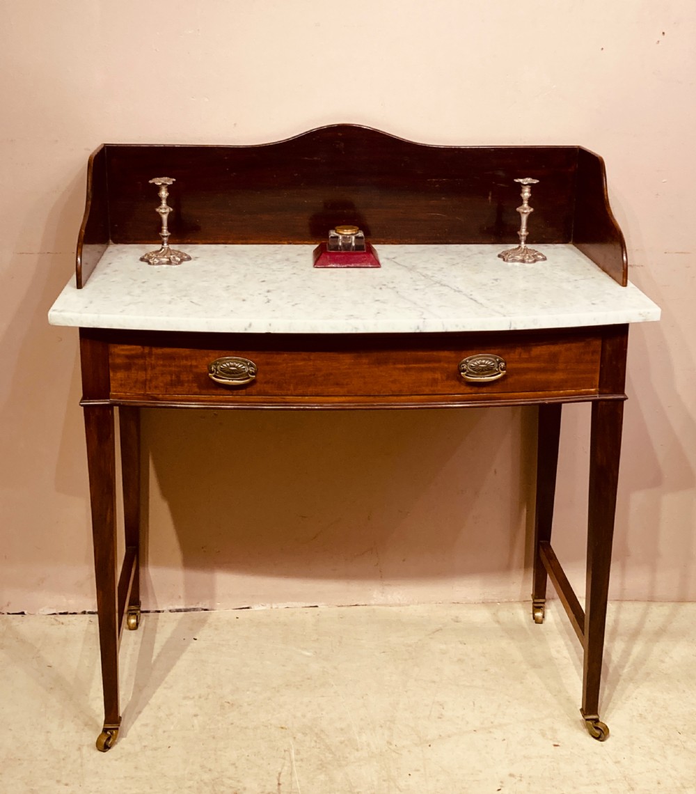 A 19th-century mahogany bow-fronted side table featuring a white marble top, a wooden gallery back, a single drawer with brass handles, and slender tapered legs on castors. View II
