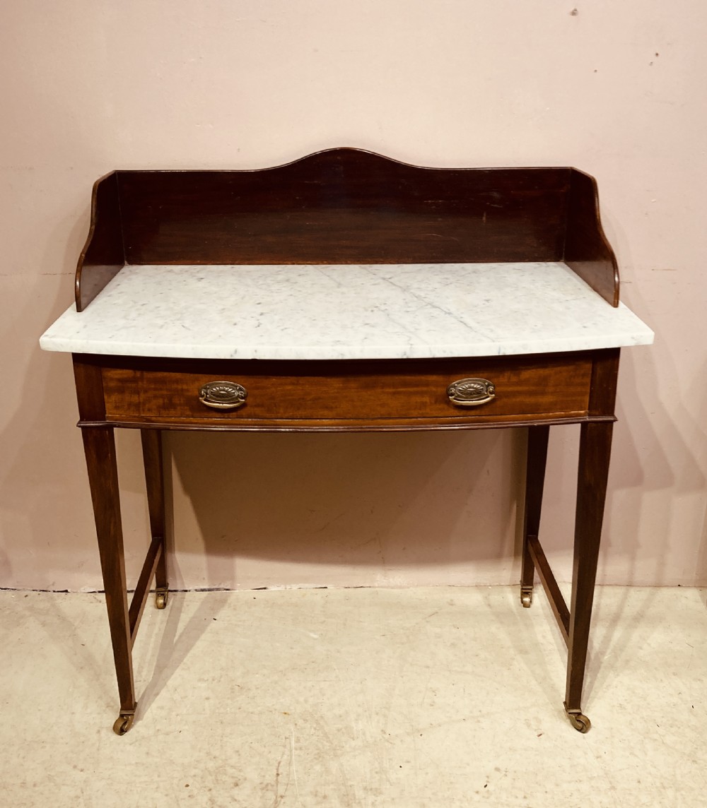 A 19th-century mahogany bow-fronted side table featuring a white marble top, a wooden gallery back, a single drawer with brass handles, and slender tapered legs on castors. View IX