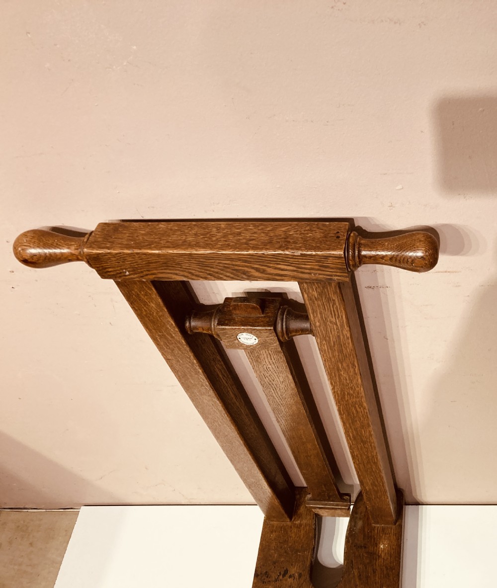 An antique freestanding oak boot jack featuring two top handles, a central vertical column, and a heel removal slot at the base. View IV