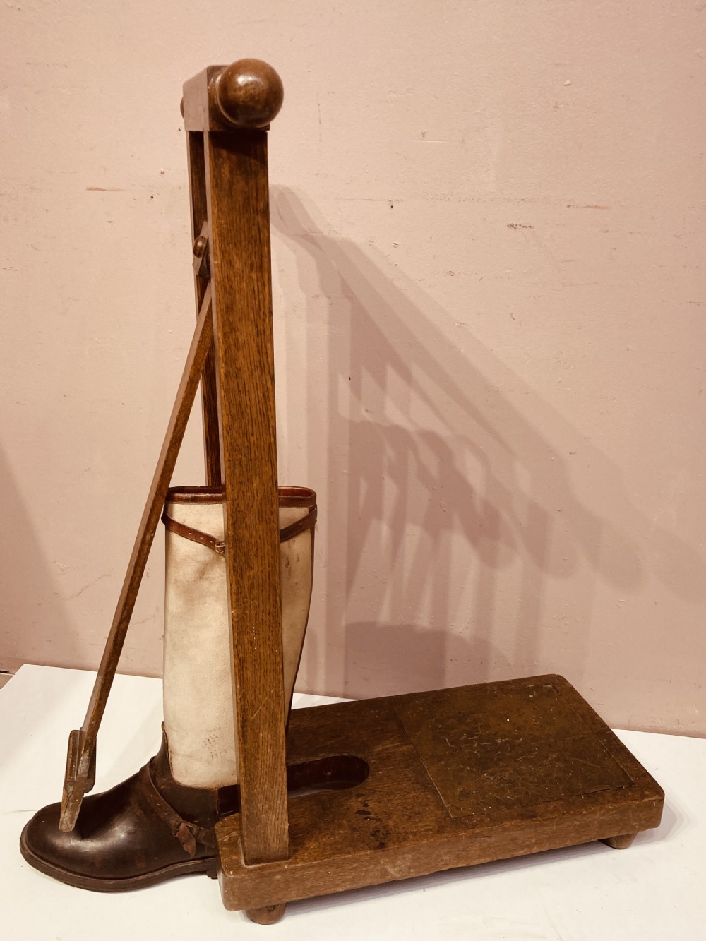 An antique freestanding oak boot jack featuring two top handles, a central vertical column, and a heel removal slot at the base. View IX
