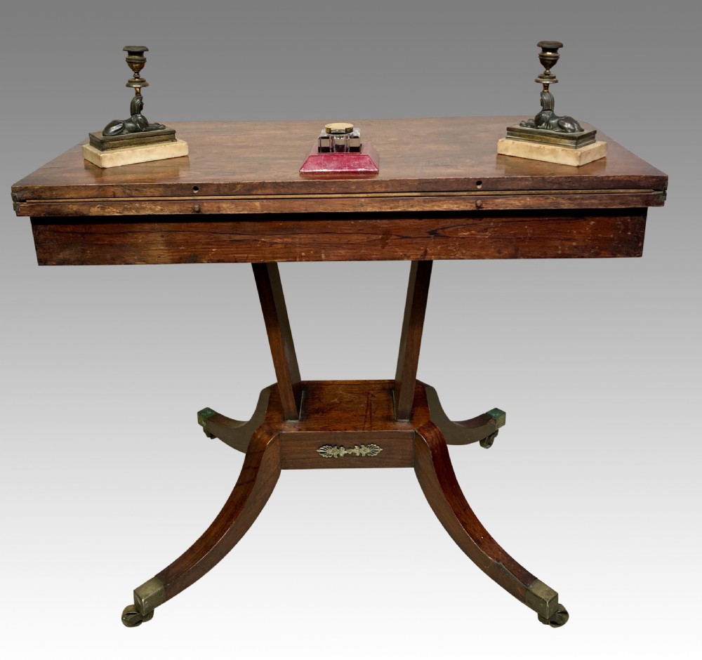 A Regency rosewood fold-over card table featuring brass inlay, a central pedestal support, and four curved sabre legs on brass castors. View IV