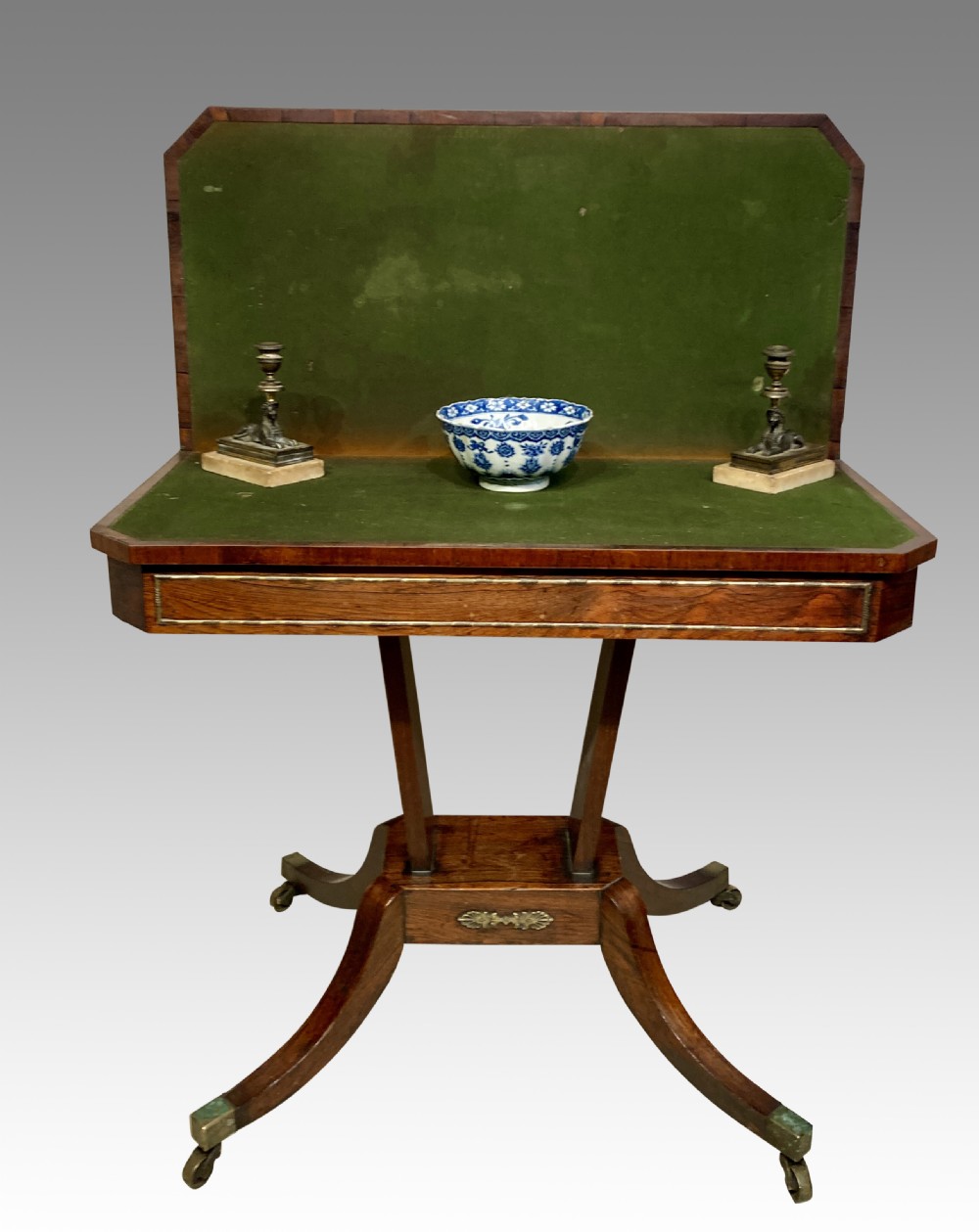 A Regency rosewood fold-over card table featuring brass inlay, a central pedestal support, and four curved sabre legs on brass castors. View VI